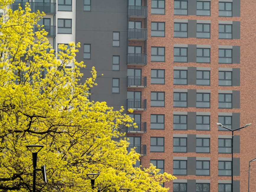 Photograph of two multi-storey residential buildings in Tufnell Park under a bright blue sky with scattered clouds. The building on the left features a modern design with a blue and white facade, larg